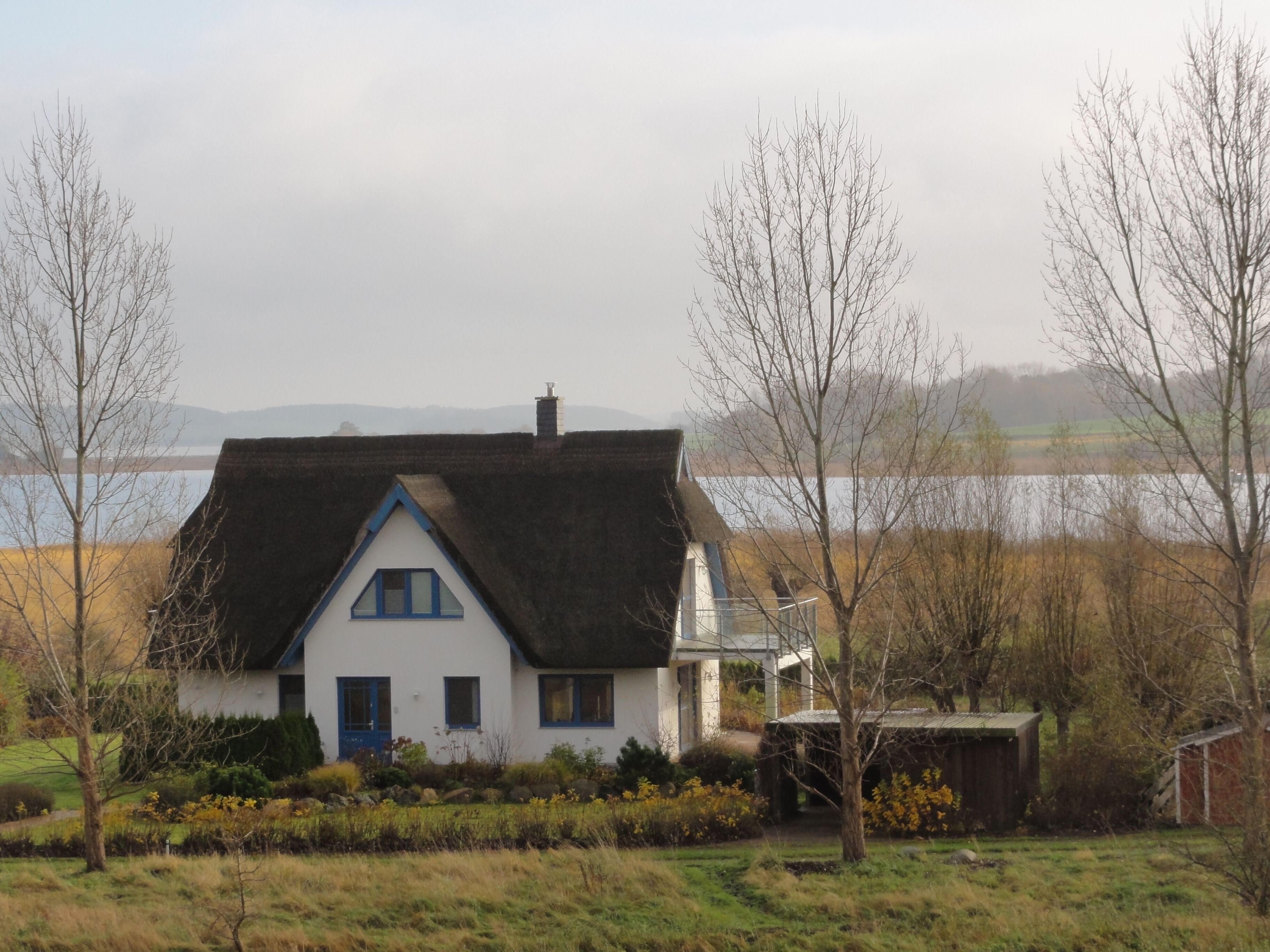 Une maison blanche avec un toit sombre, entourée d’arbres et d’un champ.