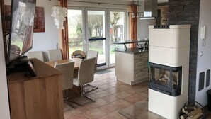 Eine moderne Küche mit eingebautem Herd, ein Essbereich mit Tisch und Stühlen sowie ein großes Fenster mit Blick ins Freie.