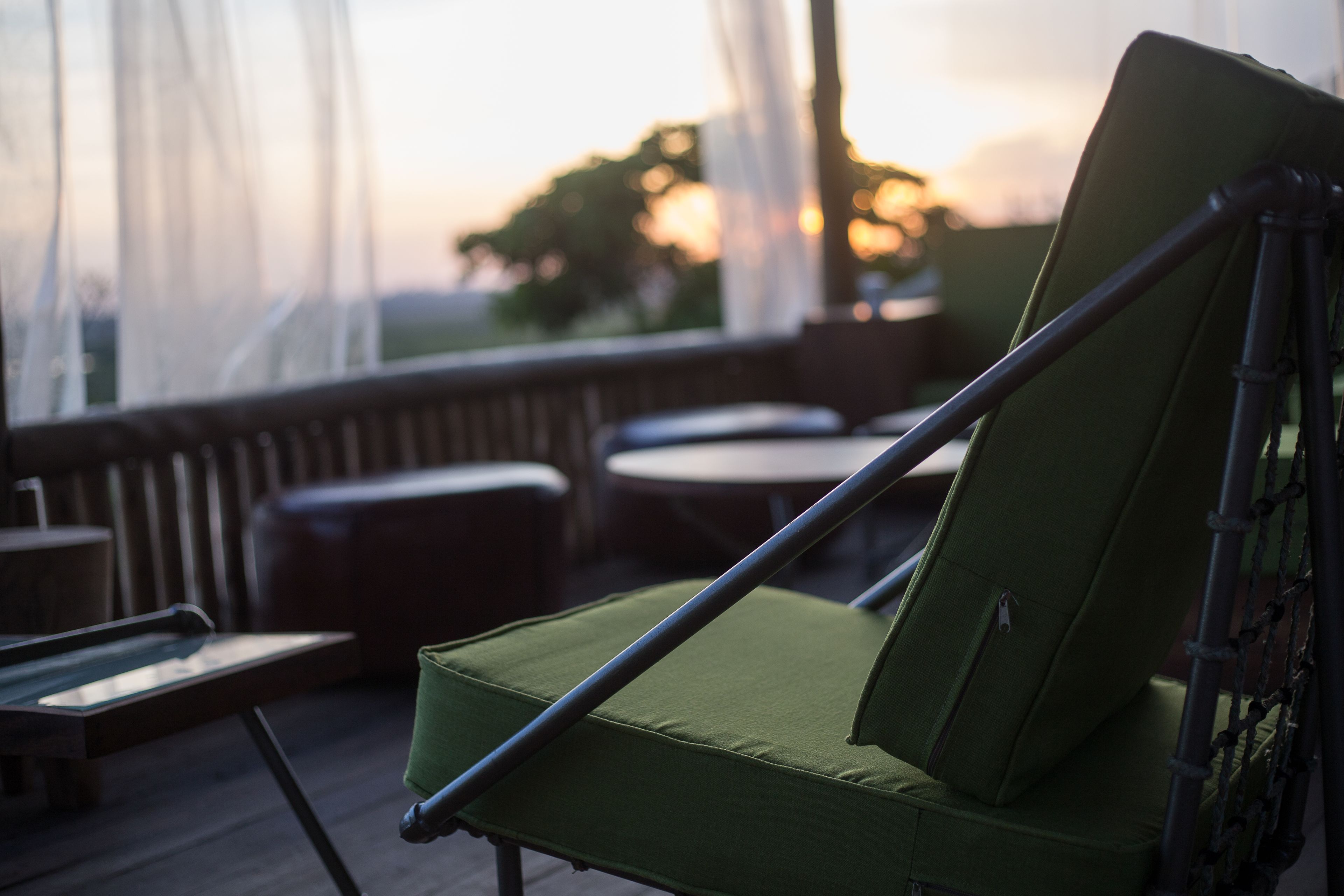 Een groene fauteuil met een metalen frame, geplaatst op een houten terras met uitzicht op de zonsondergang.