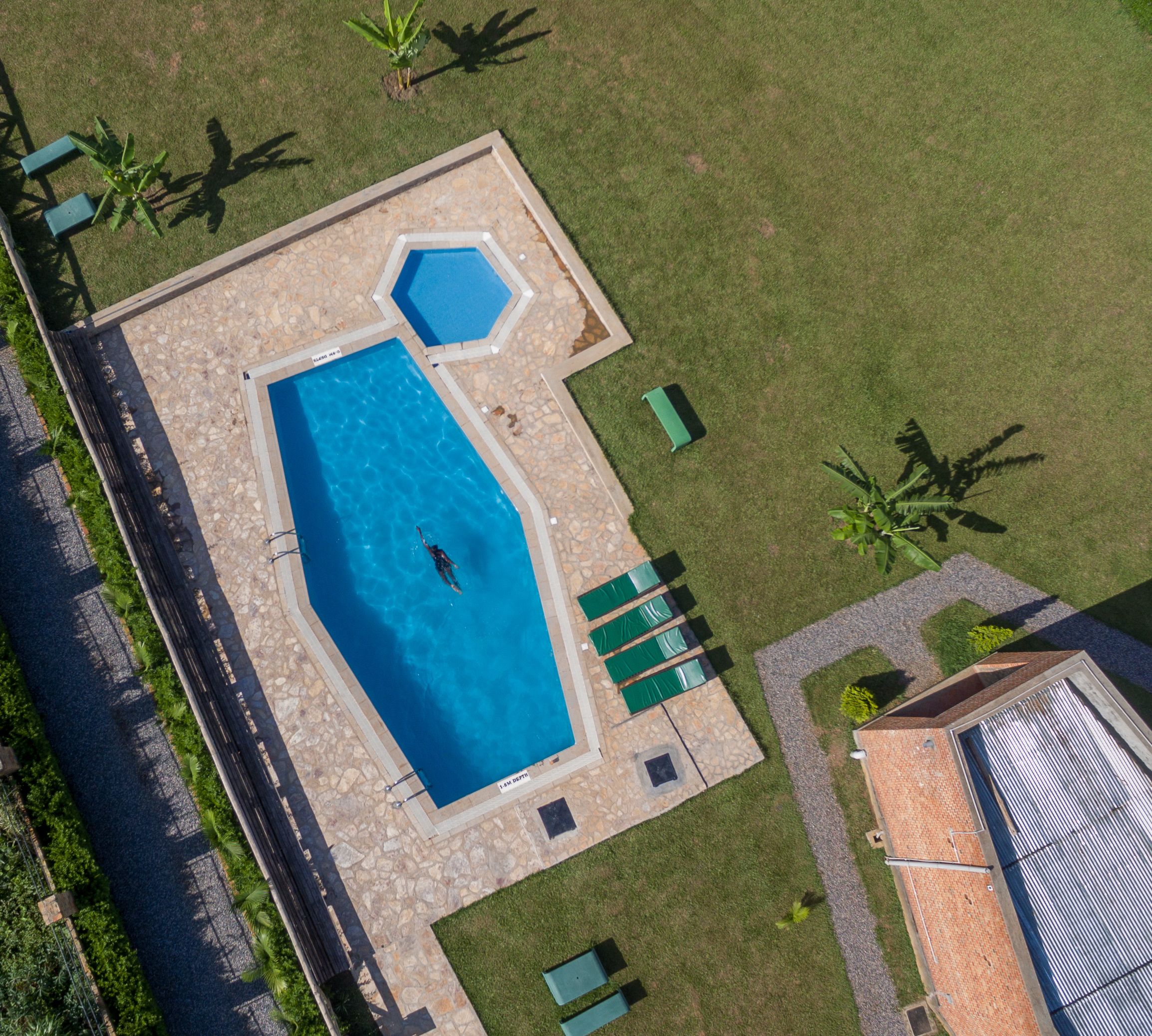 An aerial view of a swimming pool with a geometric shape, surrounded by a stone deck and green lawn.