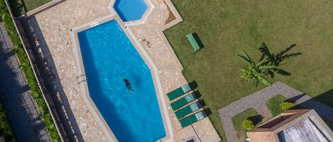 An aerial view of a swimming pool with a geometric shape, surrounded by a stone deck and green lawn.