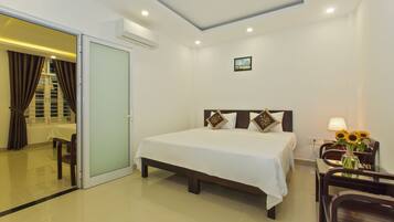 A hotel room with a bed, a desk, a chair, a vase with flowers, and a sliding door leading to a bathroom.