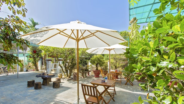 An outdoor patio area with stone flooring, wooden tables and chairs, and large white umbrellas providing shade.
