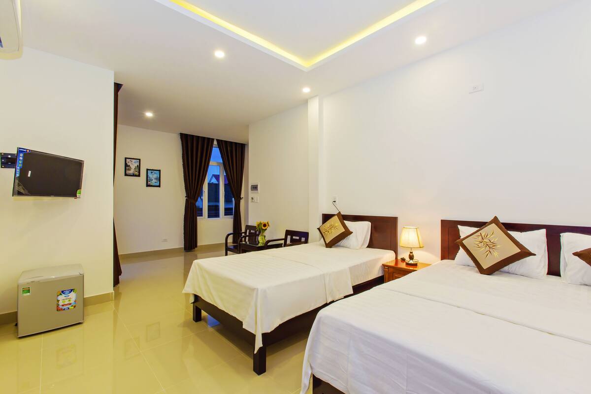 A hotel room with two beds, a TV, a desk, and a window with curtains.