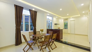 A modern dining area with a wooden table and chairs, a vase with flowers, and a kitchen in the background.