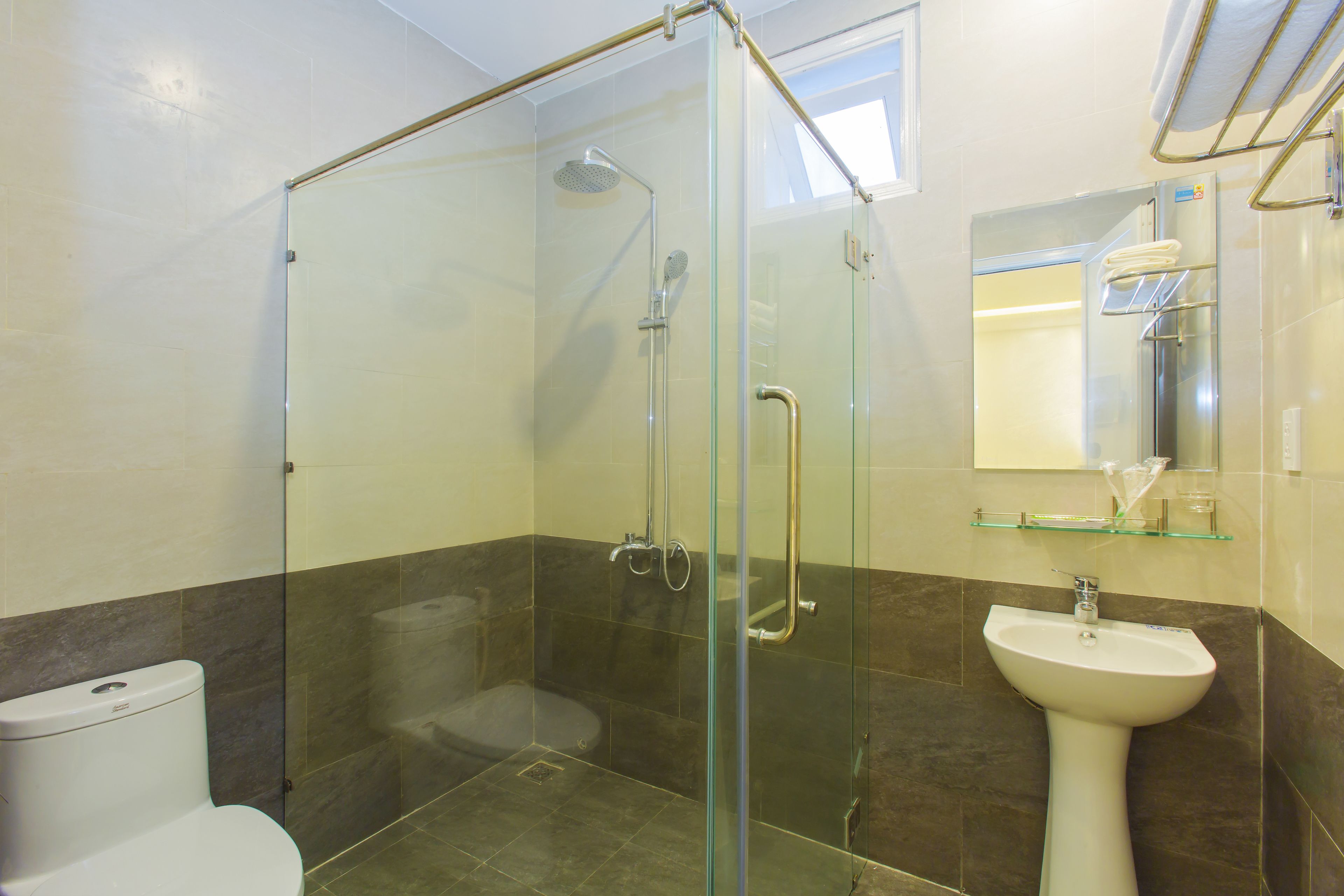 A modern bathroom with a glass-enclosed shower, a white sink, and a glass shelf above the mirror.