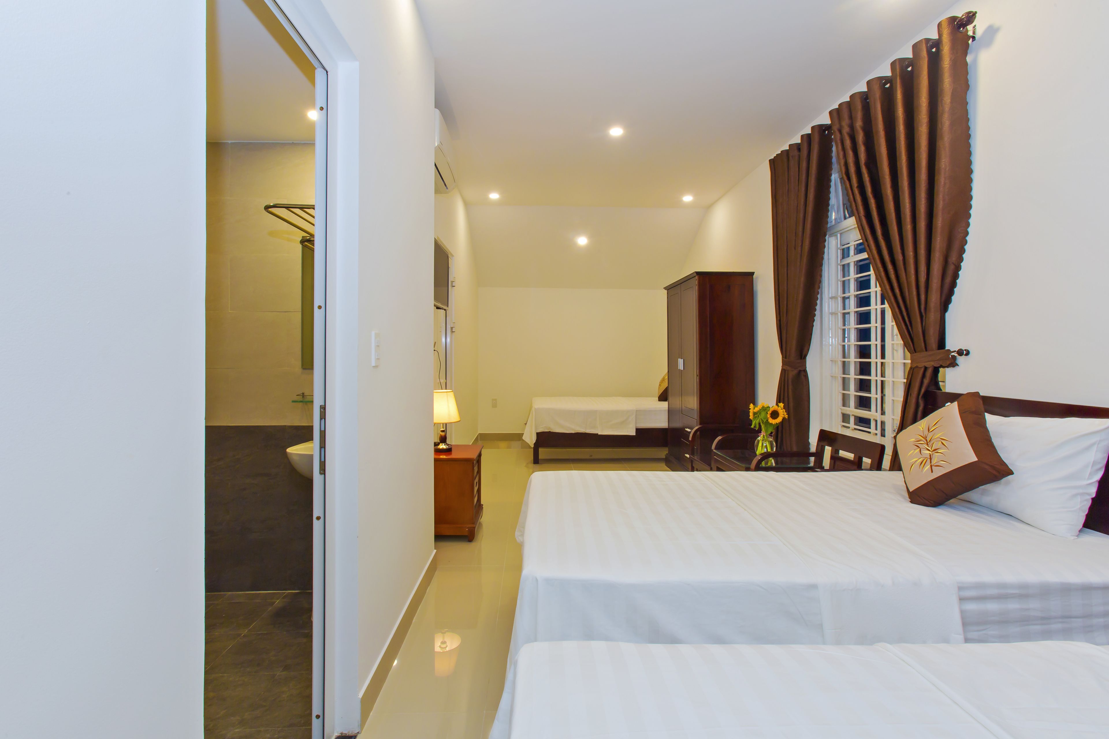 A hotel room with two beds, a bathroom, and a view of the outside.