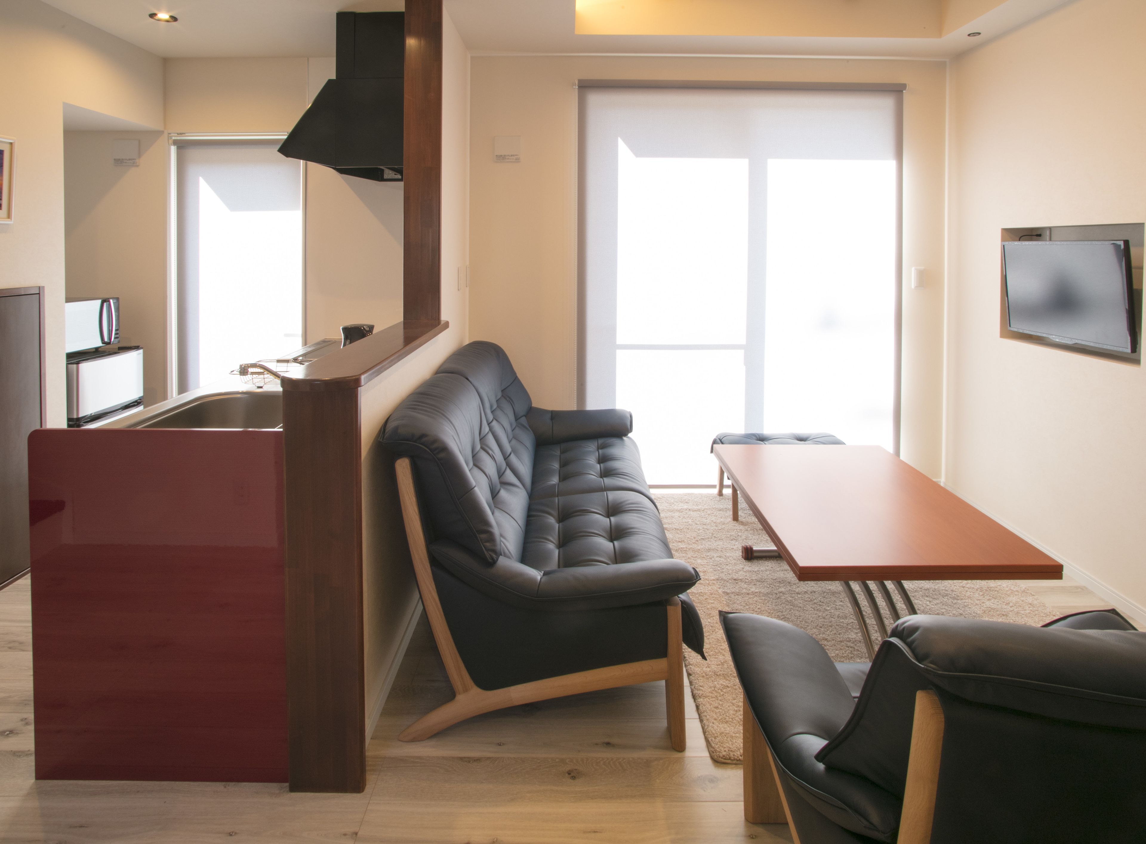 A compact living space with a kitchenette, a sofa, a dining table, and a TV mounted on the wall.