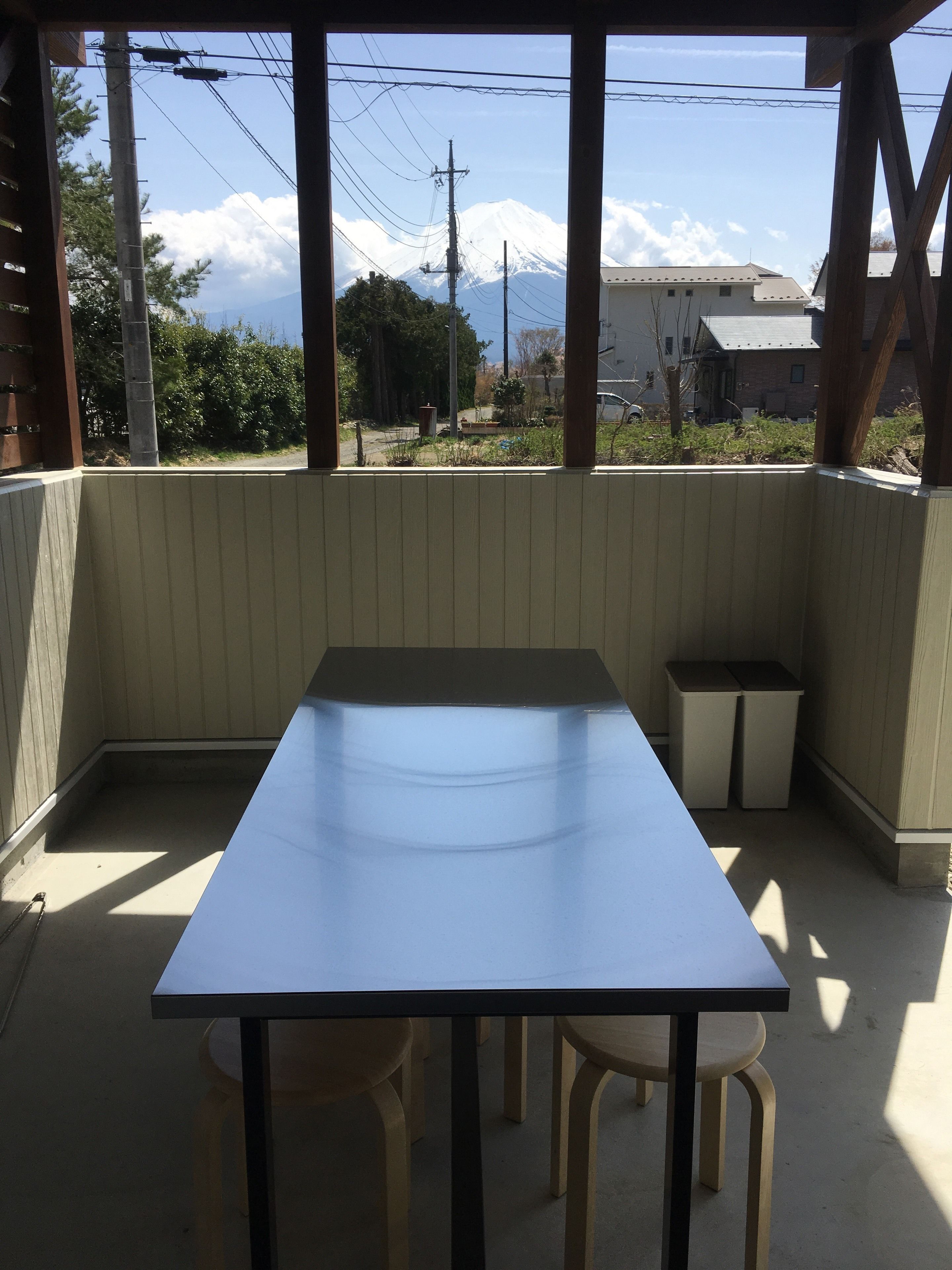 Un área de estar techada al aire libre con una mesa, sillas, un cubo de basura y vistas a una montaña nevada.
