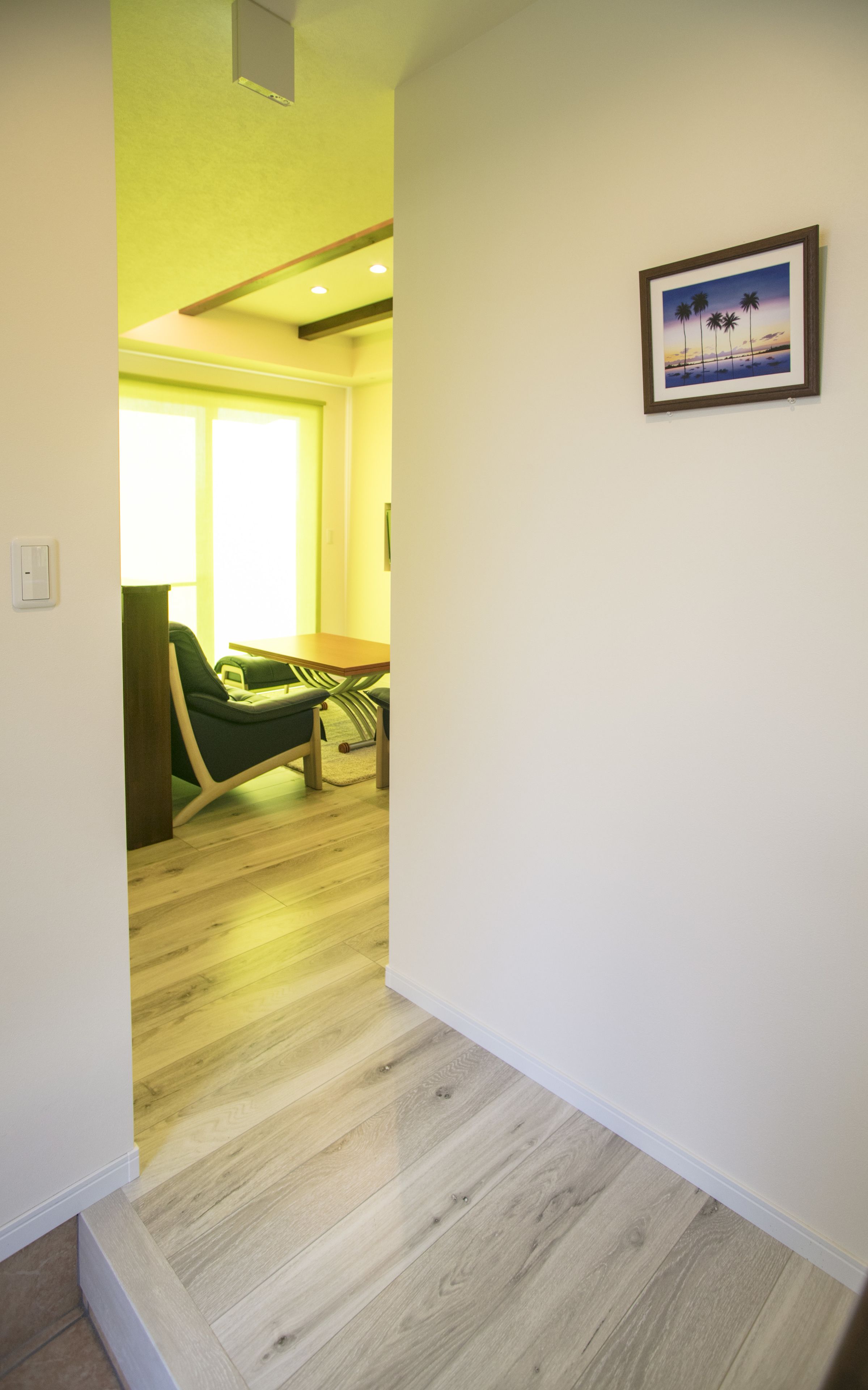 A hallway with a wooden floor, a green chair, and a framed picture on the wall.