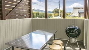 A covered outdoor area with a metal table, wooden stools, and a barbecue grill. - Villa Yushin (Fujikawaguchiko)