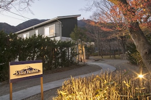 Uma villa chamada Villa Yushin, com design moderno, rodeada por árvores e com a montanha ao fundo.