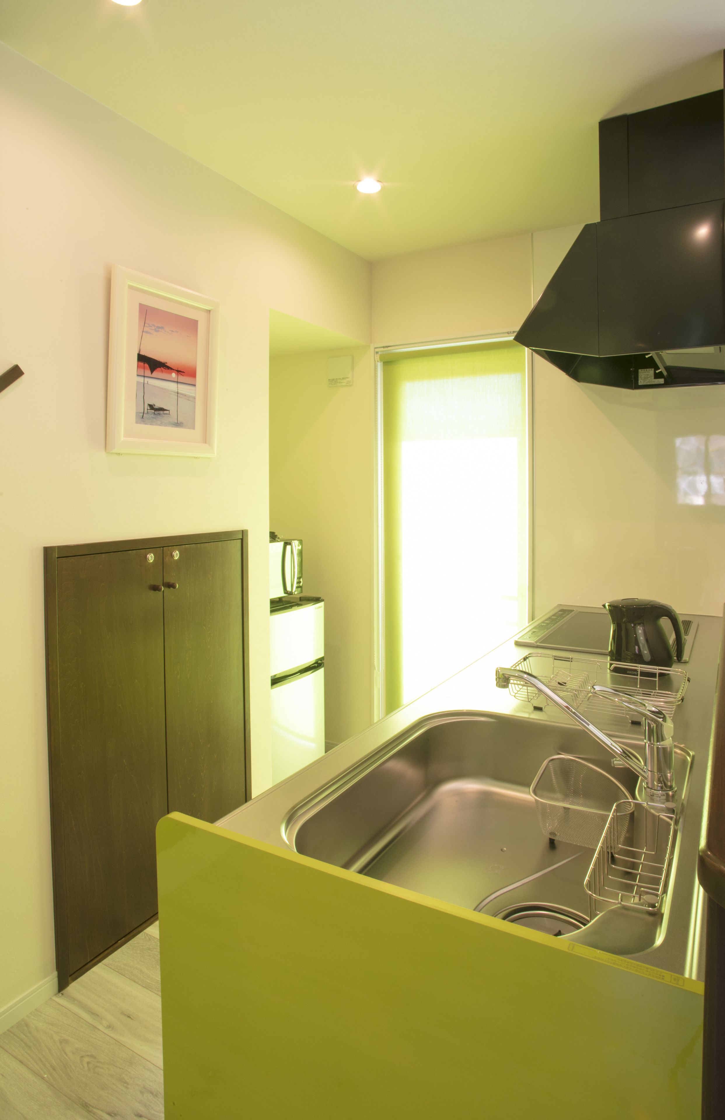 A compact kitchen with a stainless steel sink, a black range hood, and a small window.