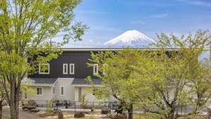 A modern house with a view of a snow-capped mountain, surrounded by trees and a patio area with outdoor furniture. - Villa Yushin (Fujikawaguchiko)