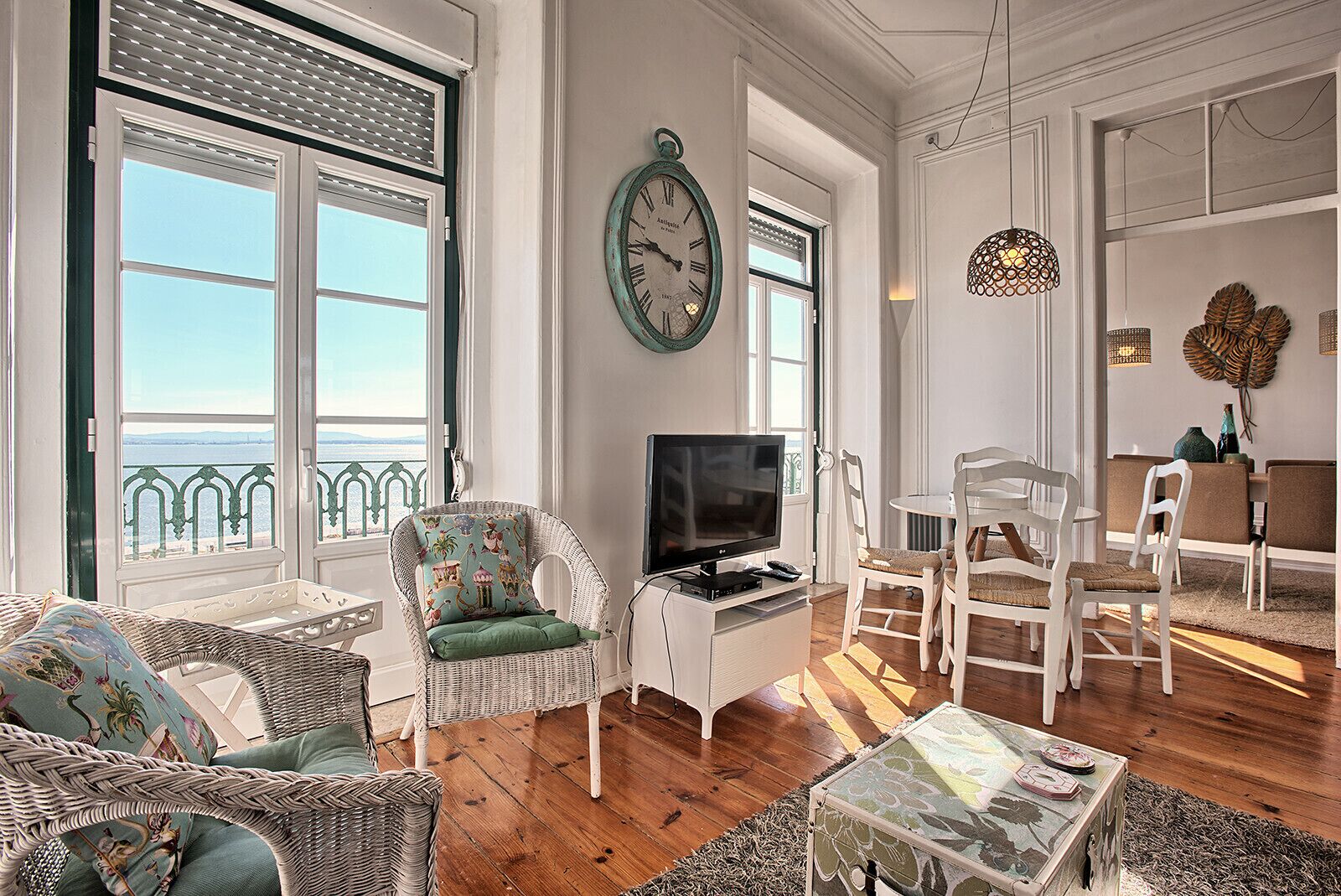 A living room with a television, wicker furniture, and a view of the sea.