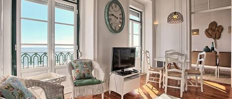 A living room with a television, wicker furniture, and a view of the sea.