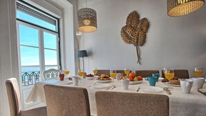 A dining area with a table set for breakfast, including plates, cups, and a fruit bowl. - Tejo I + II (Lisboa ciudad)