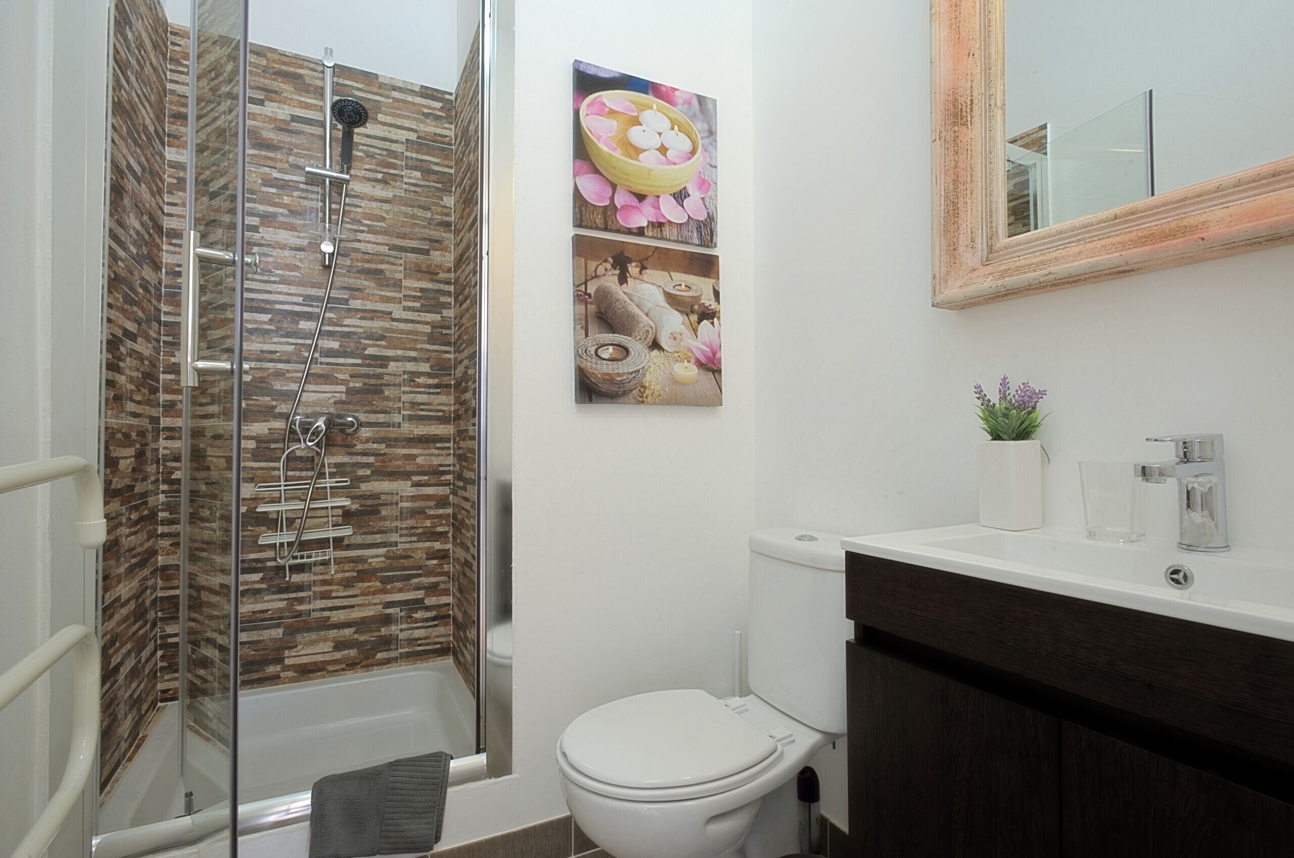 A bathroom with a glass-enclosed shower, a white toilet, and a sink with a mirror above it.