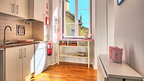 A compact kitchen with a wooden countertop, a built-in dishwasher, and a window with a view of a house. - Tejo I + II (Lisboa ciudad)