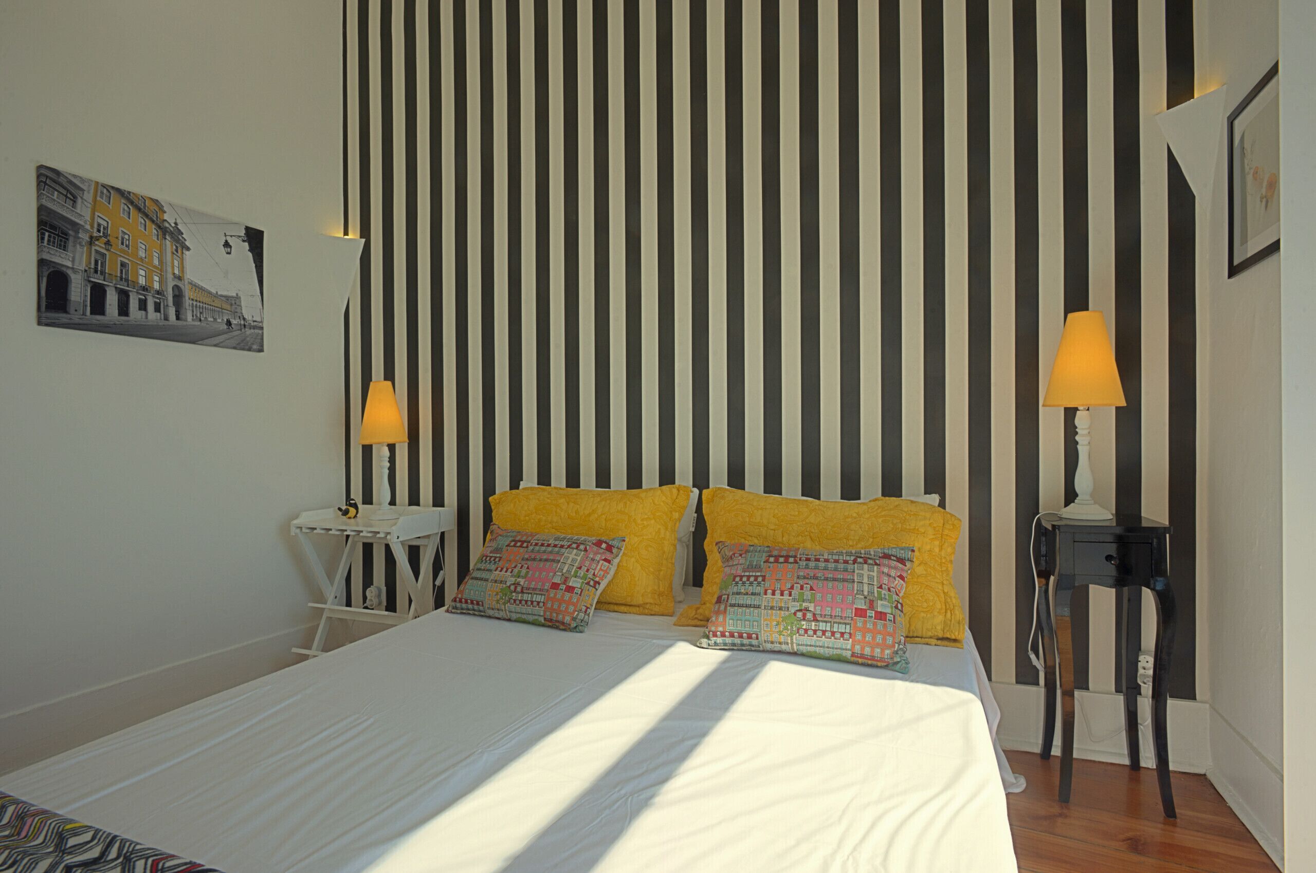 Une chambre d’hôtel avec un lit, deux lampes de chevet, une petite table et un tableau accroché au mur.