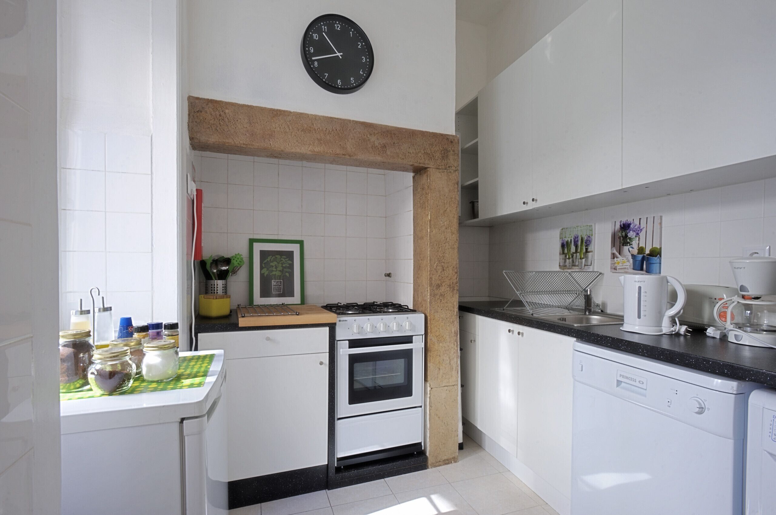 A kitchen with white cabinets, a black clock, a stove, and a coffee maker.