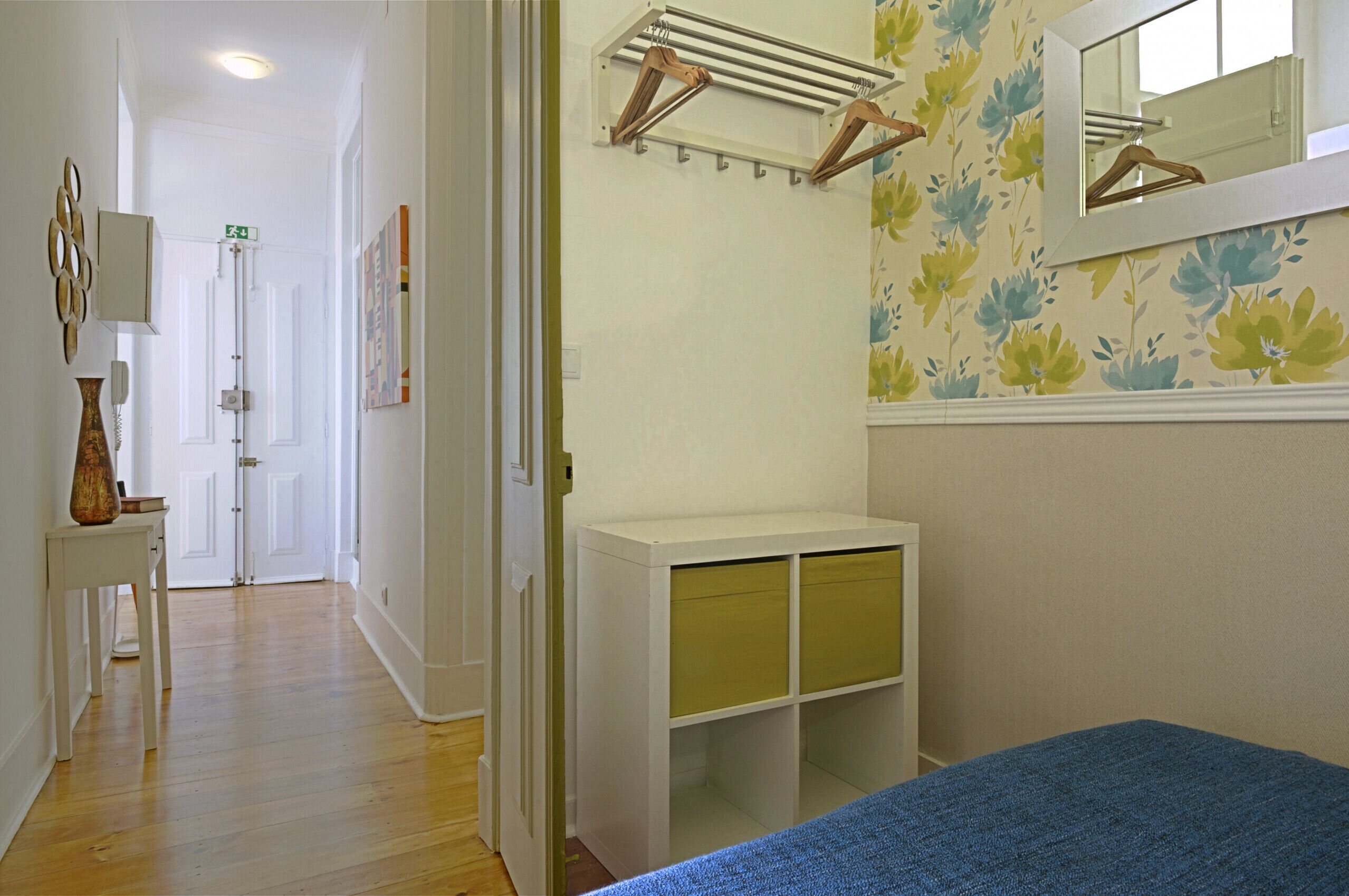 A bedroom with a bed, a white dresser, a mirror, and a wall-mounted drying rack.