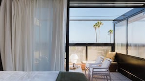 Une chambre d’hôtel moderne dotée d’un grand lit, d’un balcon avec un coin salon et d’une vue sur les palmiers.