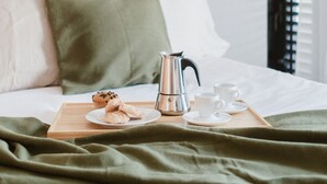 Un lit bien fait, avec un oreiller vert, un plateau sur lequel se trouvent une cafetière, des muffins et deux tasses.