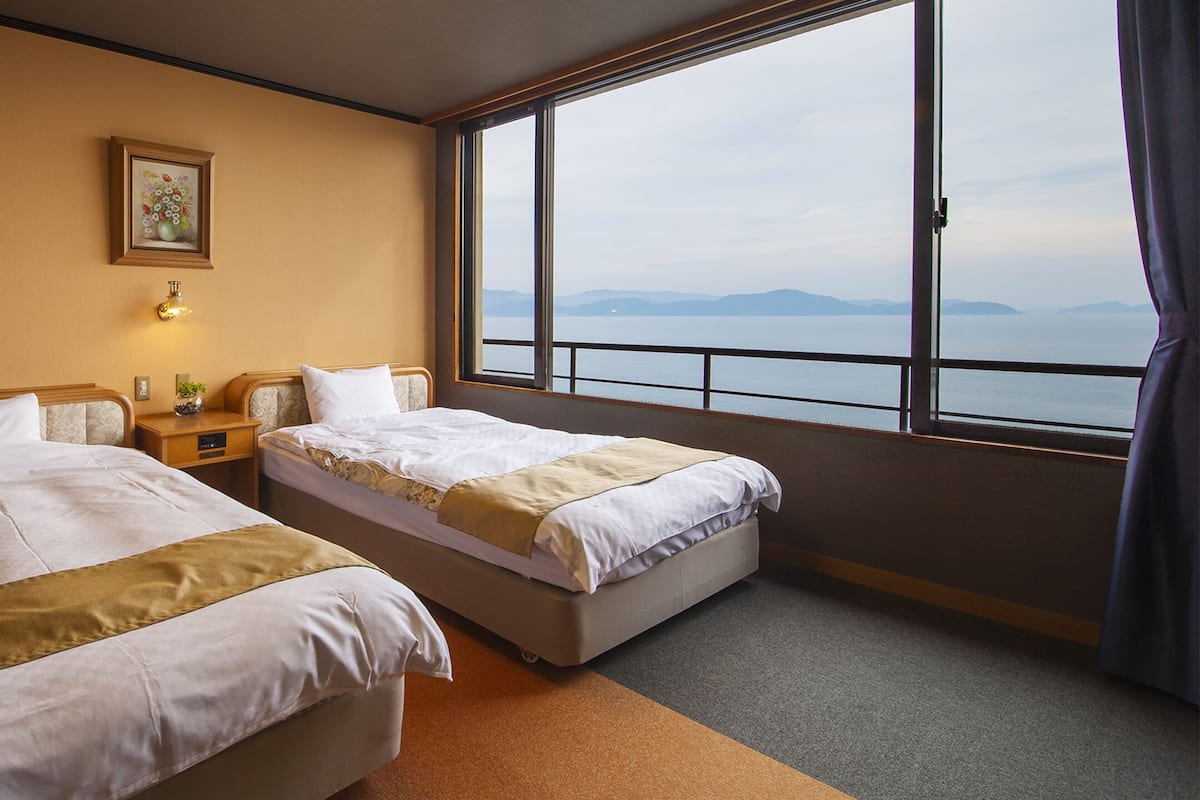 Habitación de hotel con dos camas, un ventanal con vistas al mar y un cuadro en la pared.