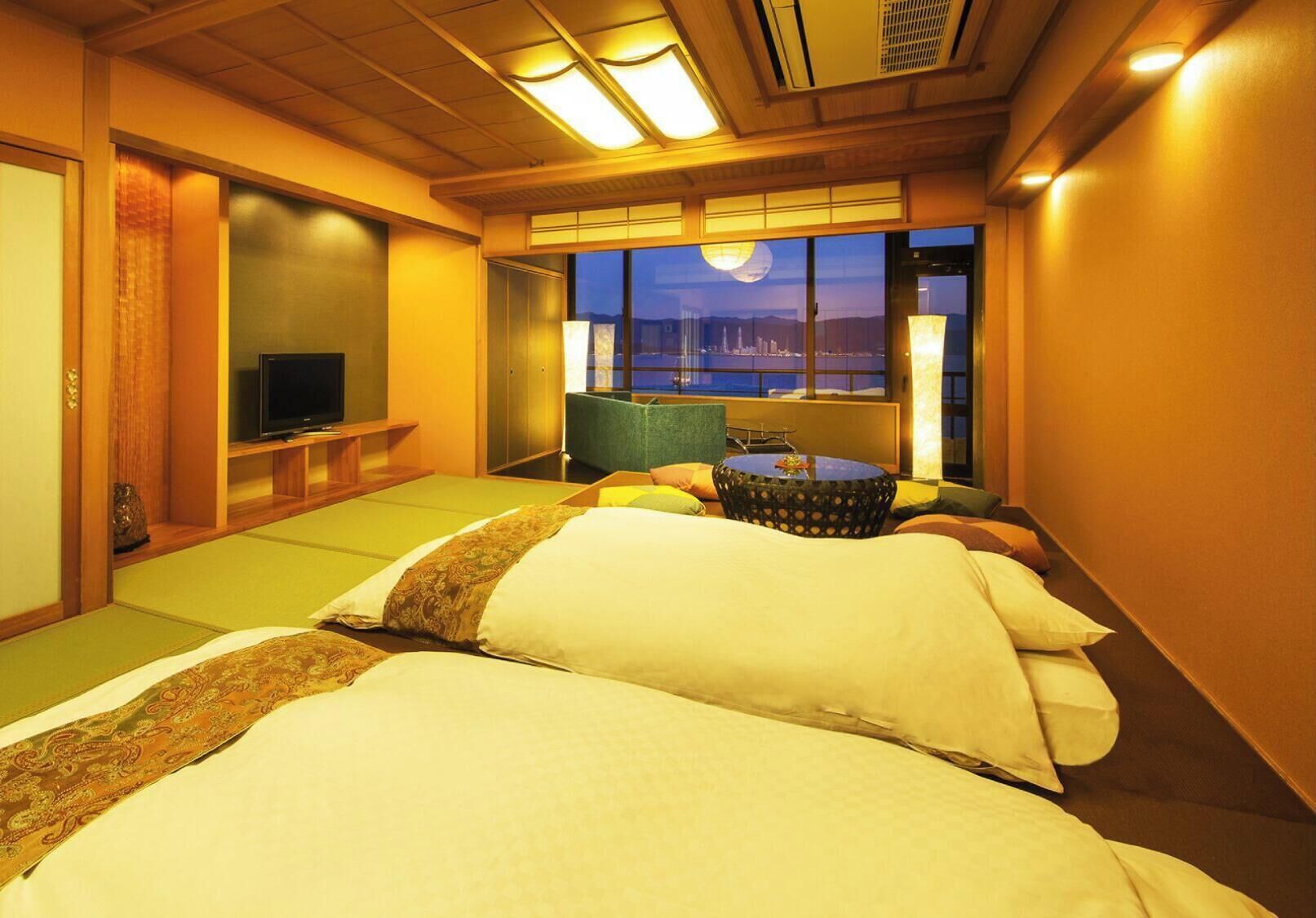 A hotel room with a bed, a television, a view of the cityscape, and a window with a moon.