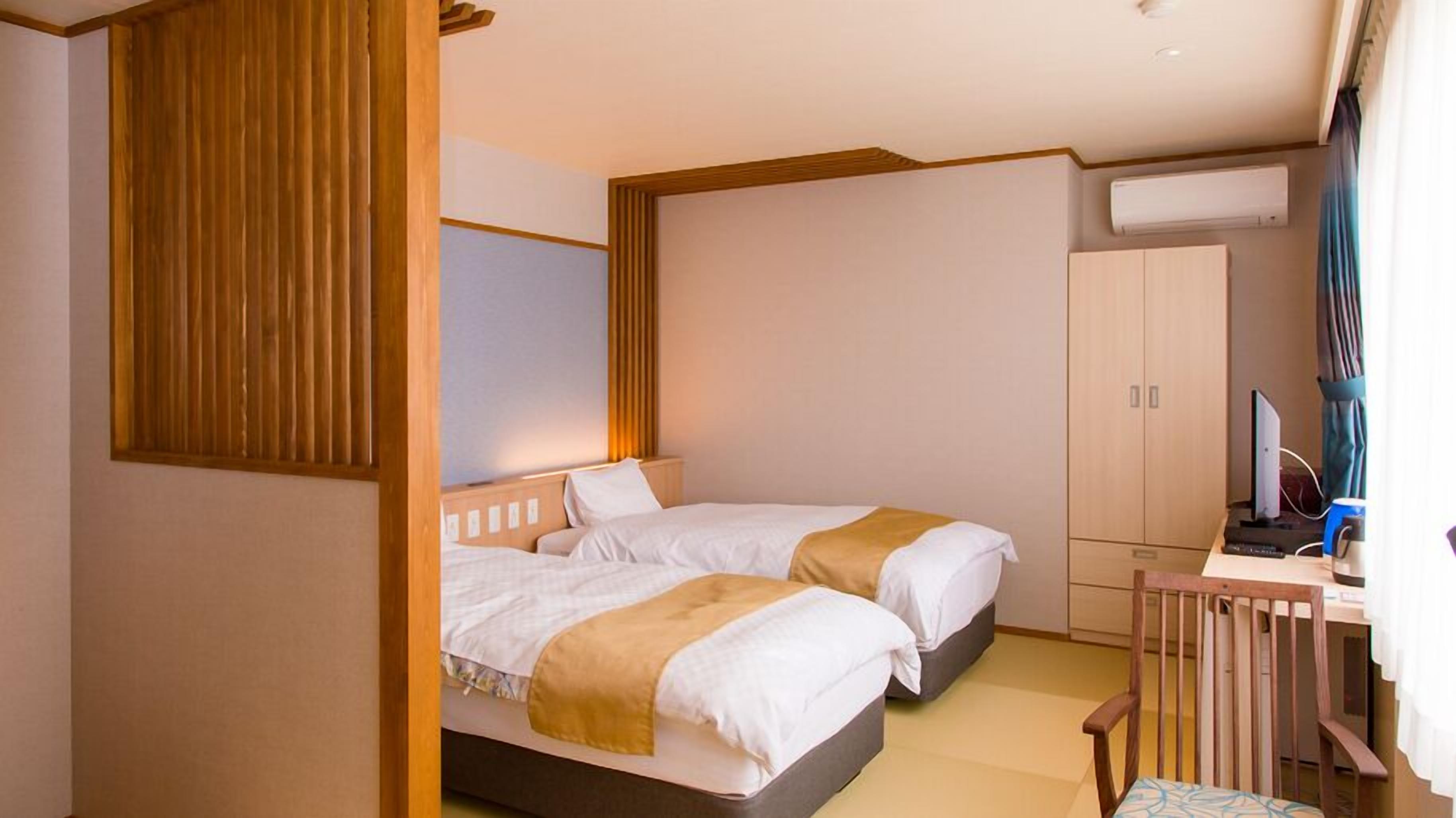 A hotel room with two beds, a desk with a computer, and an air conditioning unit.