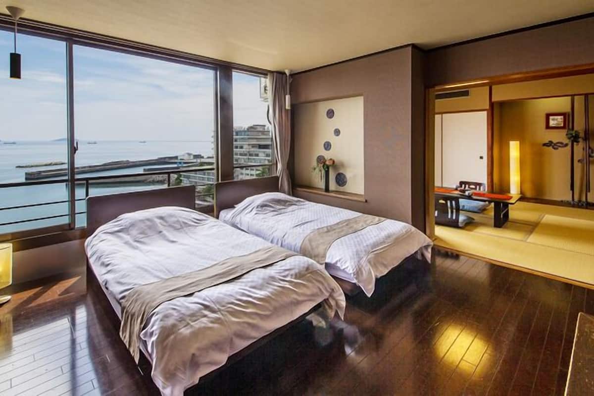 Habitación de hotel con dos camas, un ventanal con vistas al mar y una zona de estar de estilo japonés tradicional.