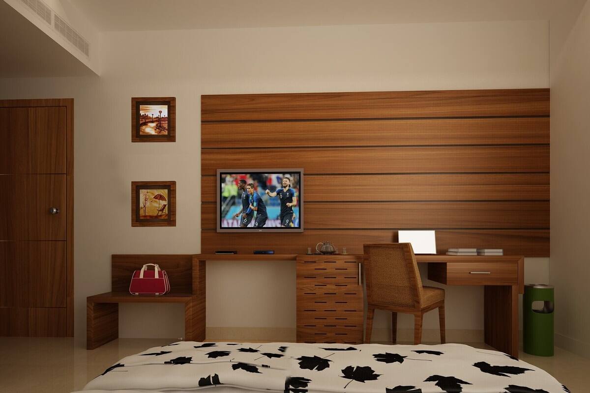 Ein modernes Schlafzimmer mit einem Holz-Kopfteil, einem an der Wand montierten Fernseher, einem Schreibtisch mit Stuhl, einem Nachttisch und einem Bett mit einem blattbedeckten Bett.