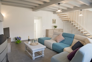 A modern living room with a staircase, a flat-screen TV, a coffee table, and a sofa.