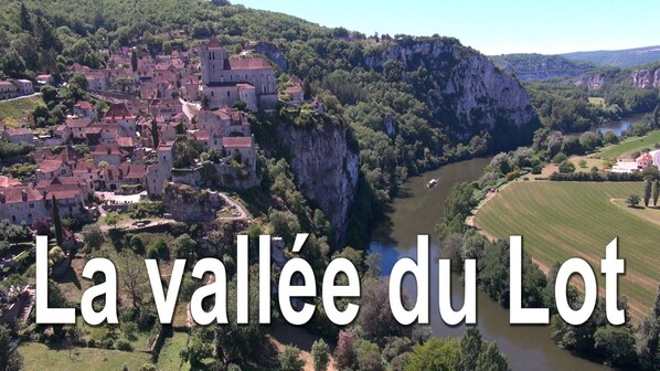 A scenic view of a valley with a river, a town with historic buildings, and a cliff.