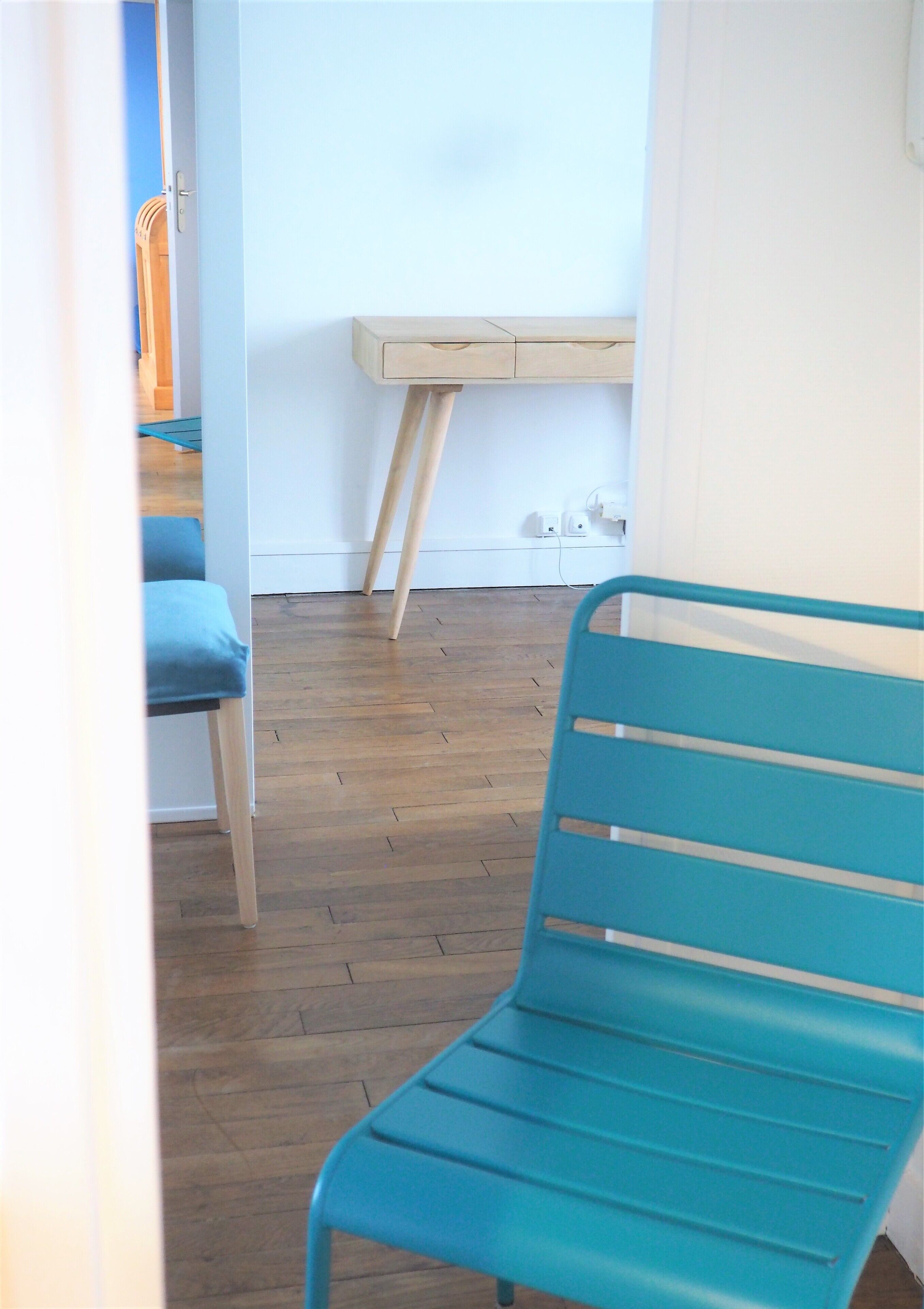 Une pièce avec un plancher en bois, une chaise bleue, un bureau en bois et un mur bleu.