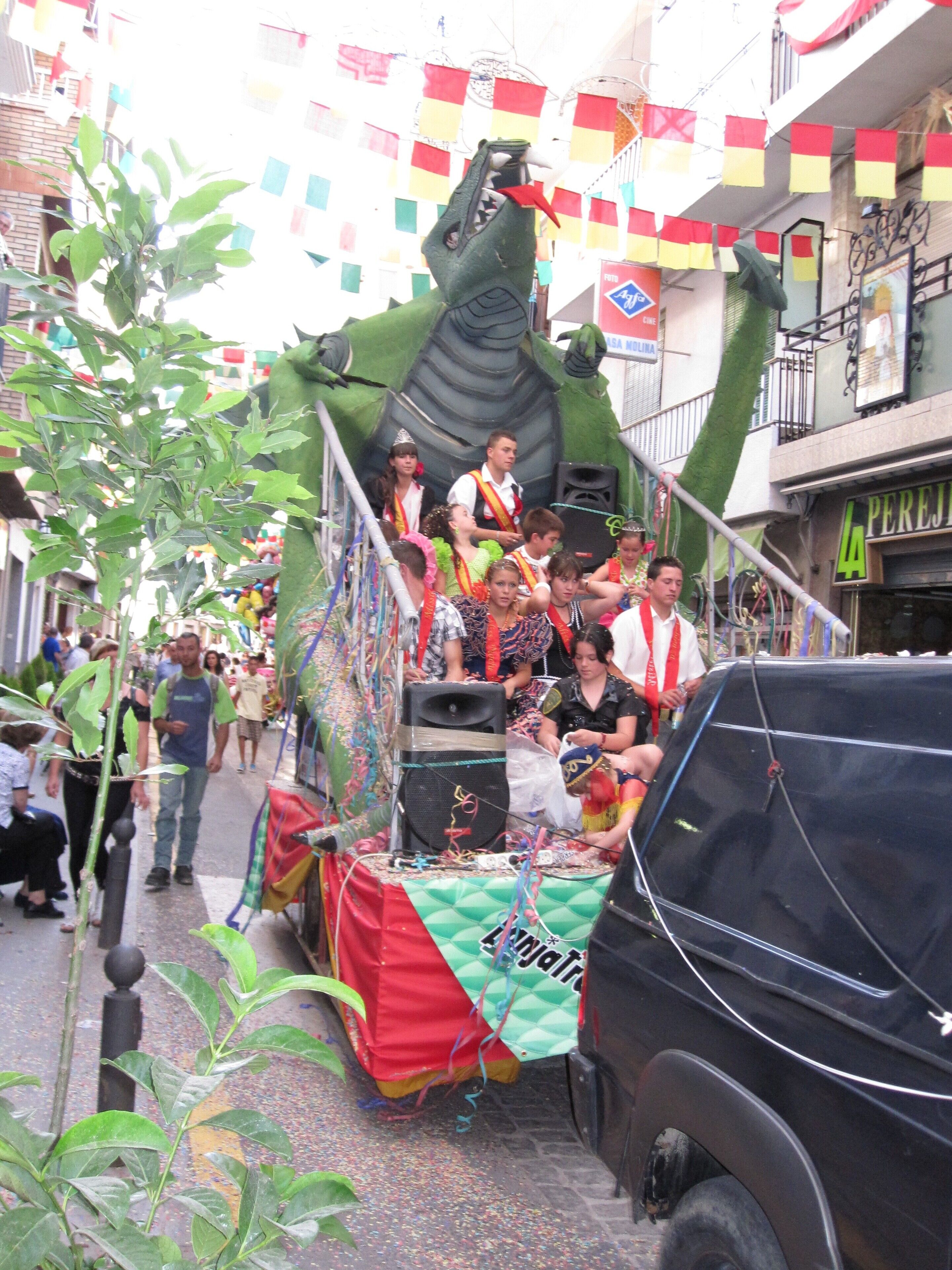 A parade float with a green dinosaur and people on it.