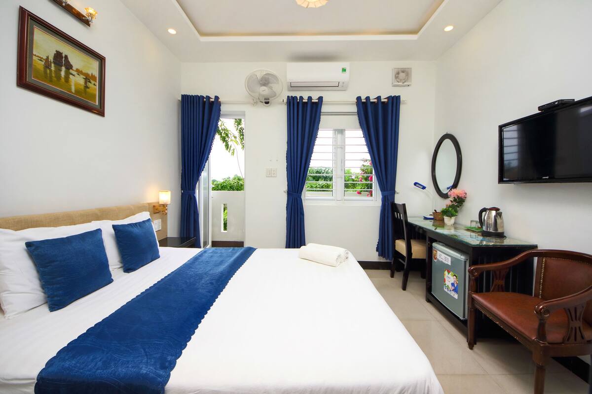 A hotel room with a large bed, a desk with a computer, a television, and a small refrigerator.