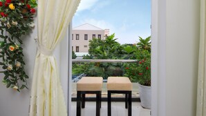 A balcony with two wooden chairs, a potted plant, and a view of a building and greenery. - Flame Flowers Homestay (Da Nang)