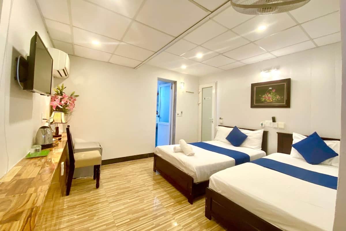 A hotel room with two beds, a desk, a chair, a television, and a ceiling fan.