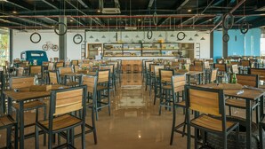 A spacious restaurant with high ceilings, exposed pipes, and a bar area. Tables are arranged in rows with chairs, and the floor is polished. - Flame Flowers Homestay (Da Nang)
