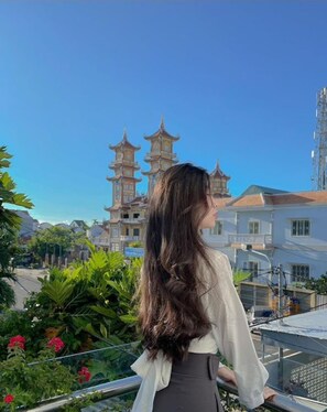 A person standing on a balcony overlooking a traditional pagoda-style building with multiple tiers. - Flame Flowers Homestay (Da Nang)