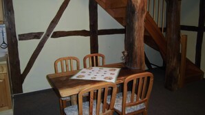 Un coin repas avec une table en bois et quatre chaises, un escalier en bois et un mur blanc avec des poutres apparentes.