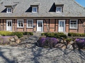 Ein traditionelles Backsteinhaus mit einem Steinweg, der zum Eingang führt, umgeben von Kies und violetten Blumen.