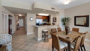 A modern kitchen with a central island, bar stools, and a dining table with wicker chairs. - 1105 - 2BR/2BA Coastal Gulf Views (Panama City Beach)