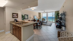A spacious living area with a kitchen, dining table, and a balcony with a view. - 1105 - 2BR/2BA Coastal Gulf Views (Panama City Beach)