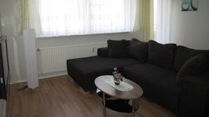 A living room with a dark-colored sofa, a small round table with a vase of flowers, and a radiator under a window with sheer curtains. - Modern and quiet apartment right in the city center of Berlin (Berlin)