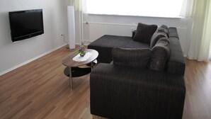 A modern living room with a dark grey sofa, a flat-screen TV mounted on the wall, and a small round table with a vase of flowers. - Modern and quiet apartment right in the city center of Berlin (Berlin)