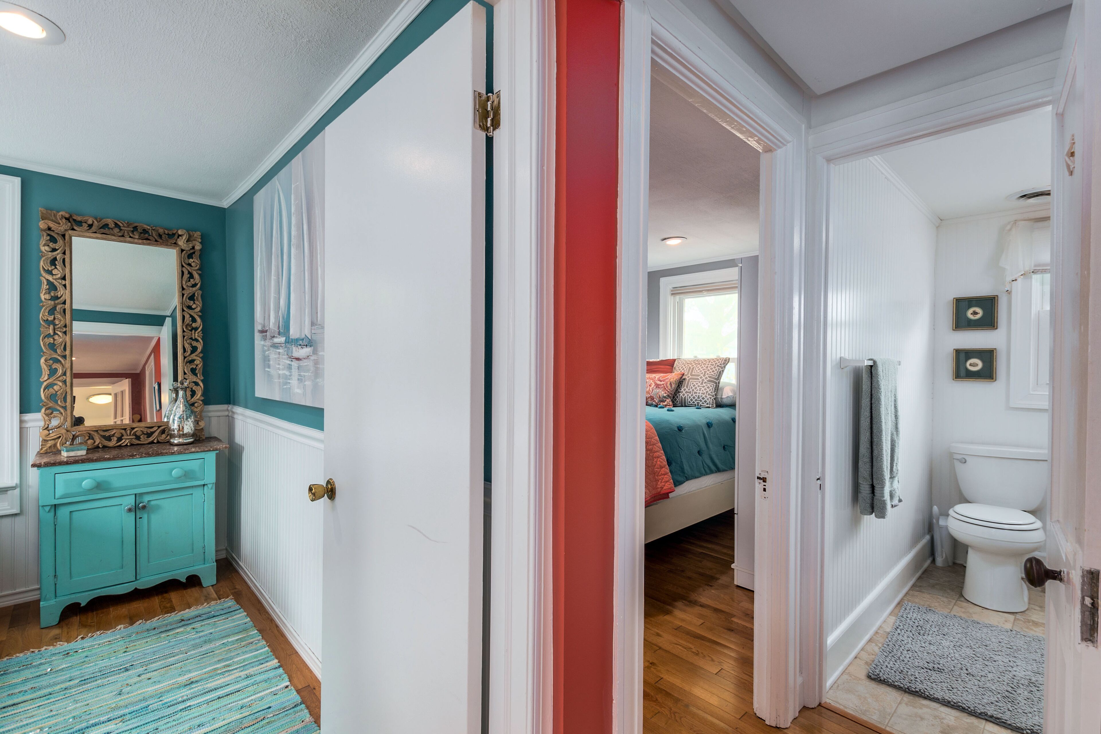 A hallway leading to a bedroom with a bed, a bathroom with a toilet, and a vanity with a mirror.
