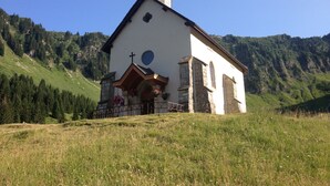 En liten kyrka med ett klocktorn, omgiven av en gräsklädd äng och berg.
